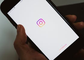 Close-up of a hand holding a smartphone displaying the Instagram app screen.